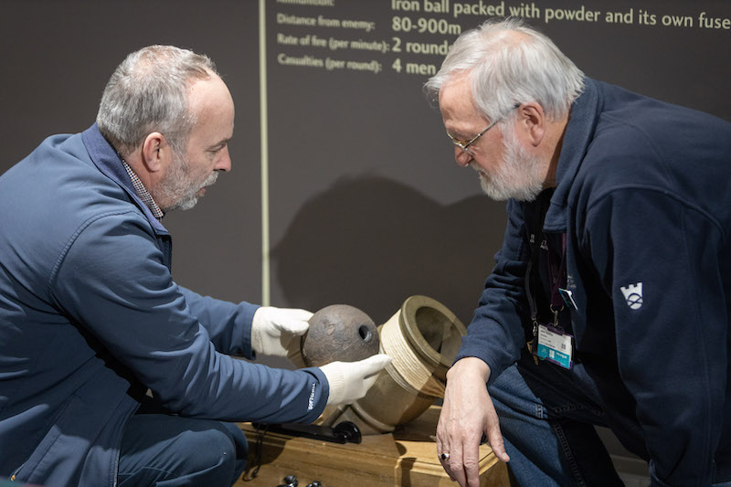 The National Trust for Scotland's Head of Archaeology, Derek Alexander, with volunteer John Easson, observing a replica Coehorn mortar. Derek holds the Coehorn mortar shell © National Trust for Scotland